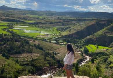 Une jeune femme se tient au bord d'une falaise surplombée une vallée malgache. Elle regarde l'horizon