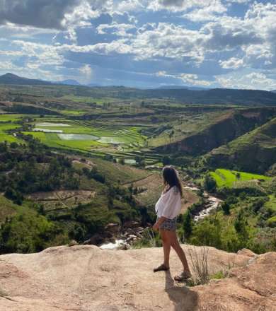 Une jeune femme se tient au bord d'une falaise surplombée une vallée malgache. Elle regarde l'horizon