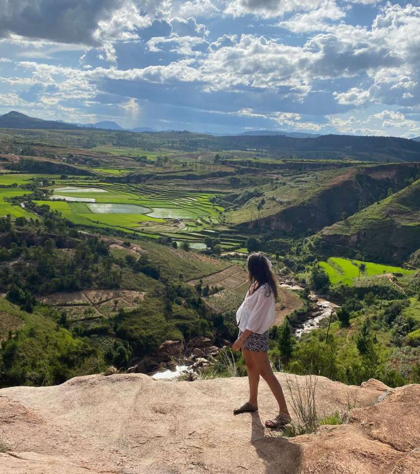 Une jeune femme se tient au bord d'une falaise surplombée une vallée malgache. Elle regarde l'horizon